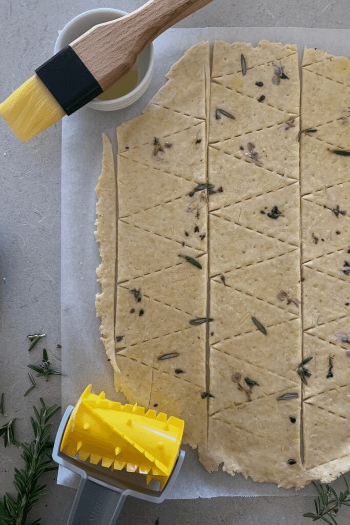 Sourdough cracker recipe dough rolled out thin and sprinkled with rosemary and salt. It has been cut with a cracker roller which is also shown in the photo.