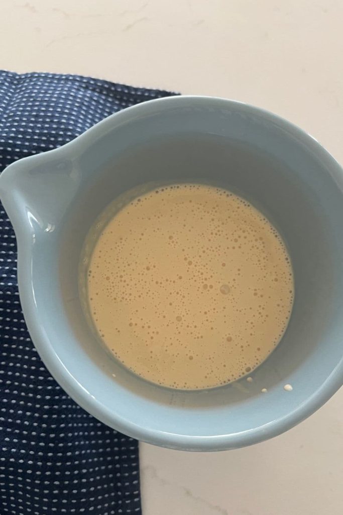 Blue mixing jug sitting on a navy blue dish towel. The jug contains sourdough popover batter.
