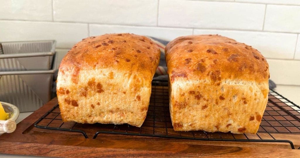 2 loaves of golden sourdough cheese bread cooling on a wire rack.