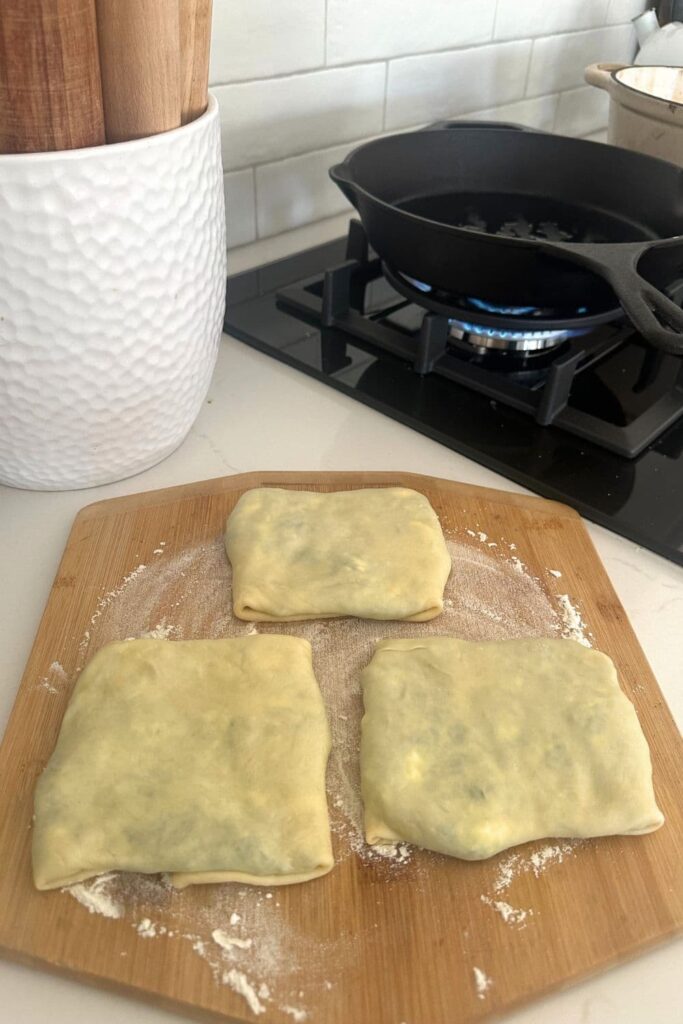 3 sourdough gozleme sitting on a wooden pizza peel waiting to be cooked in a cast iron skillet.