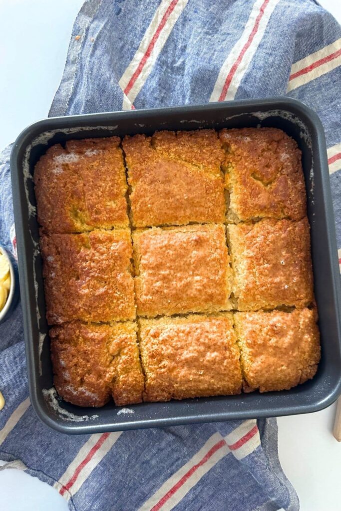 A square baking pan with 9 sourdough butter swim biscuits inside. The pan is sitting on a red, white and blue striped dish towel.