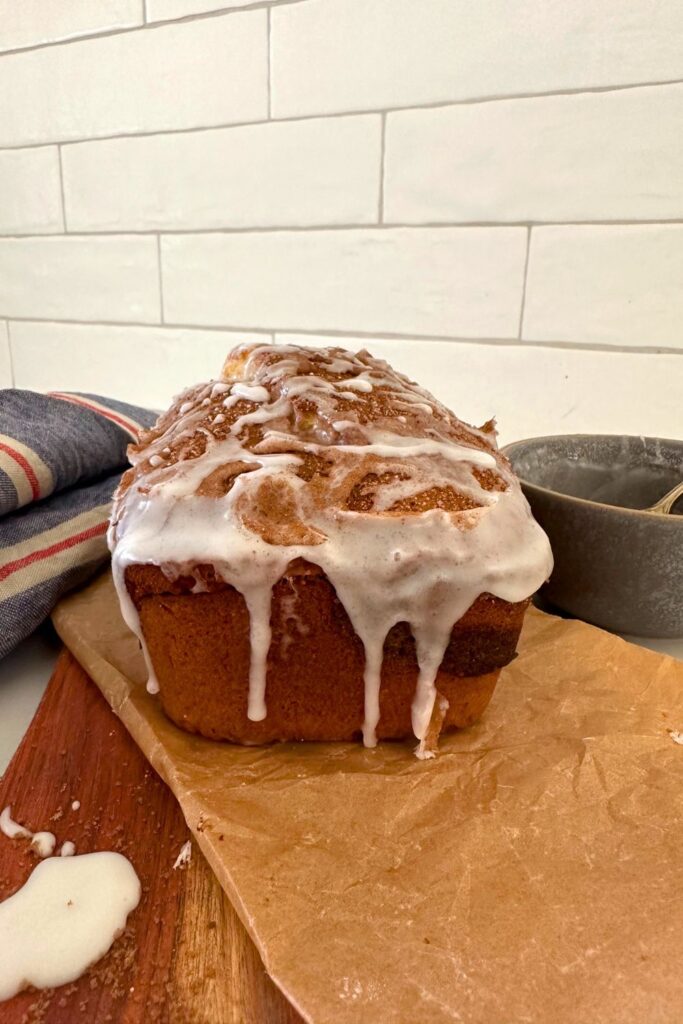 A loaf of sourdough discard cinnamon ripple quick bread drizzled in a vanilla glaze taken from one end.