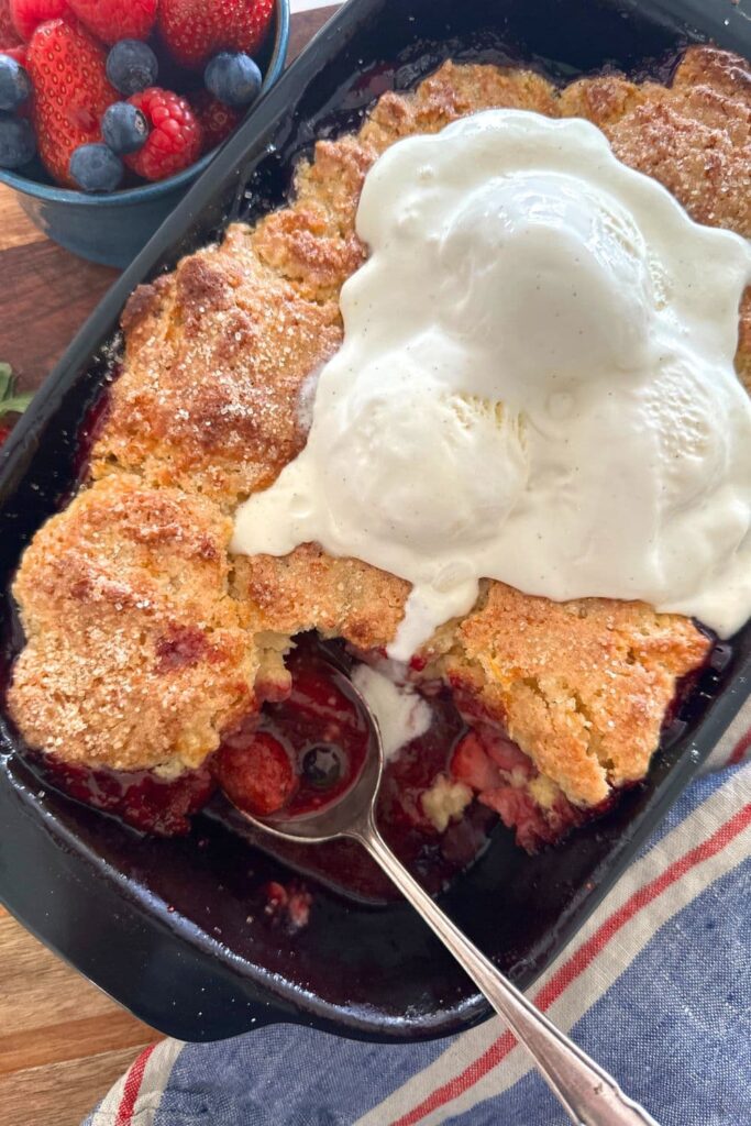 Sourdough berry cobbler baked in a black baking dish and topped with vanilla ice cream.