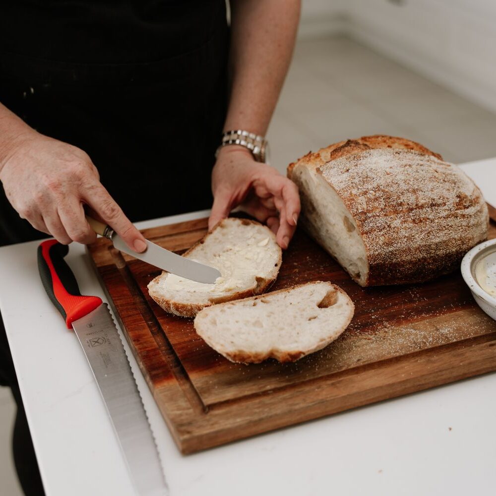 Woman's hands using a knife to spread butter on sourdough bread slices.