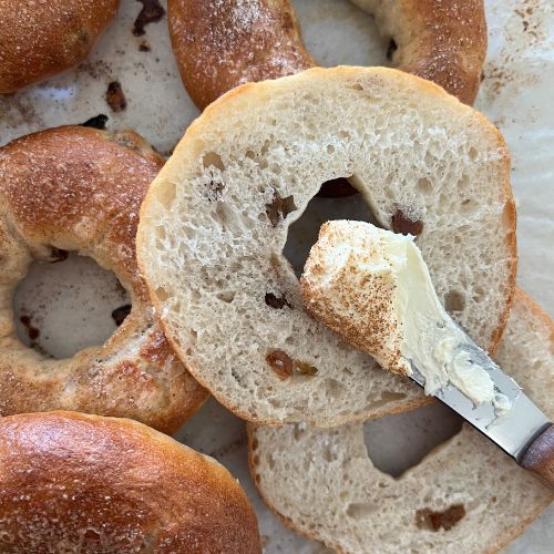 Knife spreading butter onto a sourdough bagel.